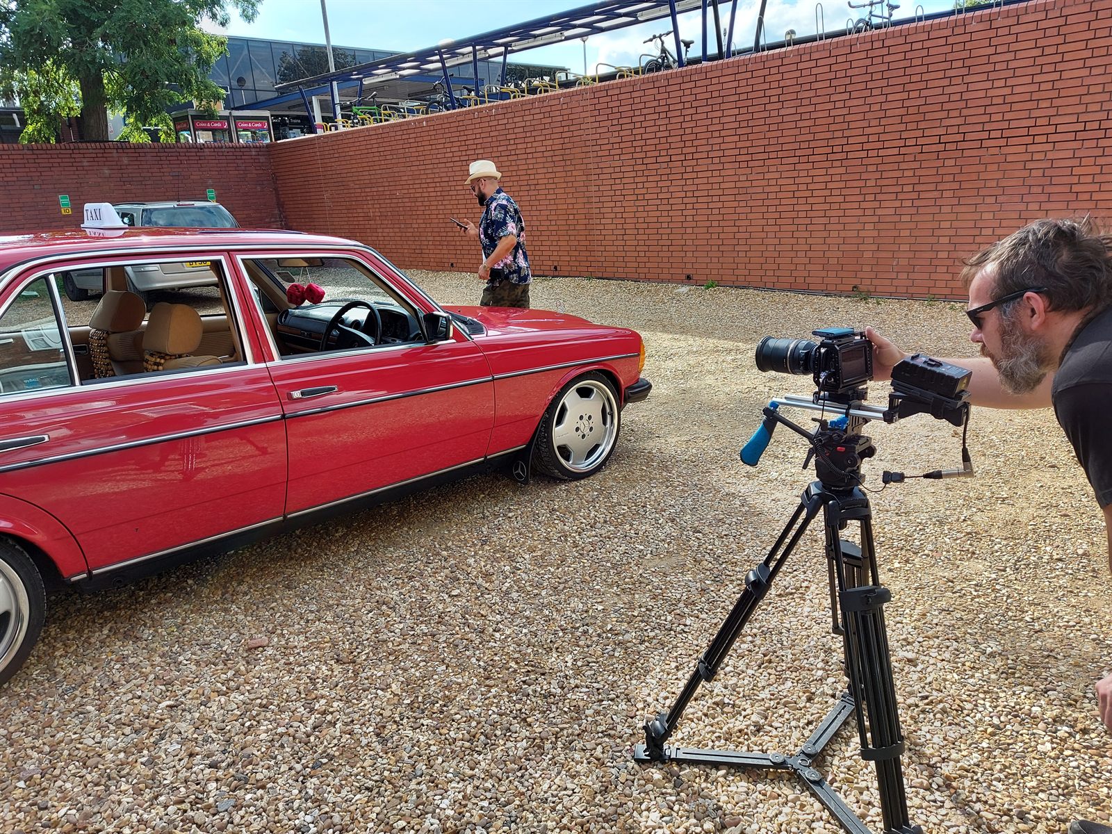 Film crew with a cinema camera on a tripod shooting the red Mercedes W123 on location