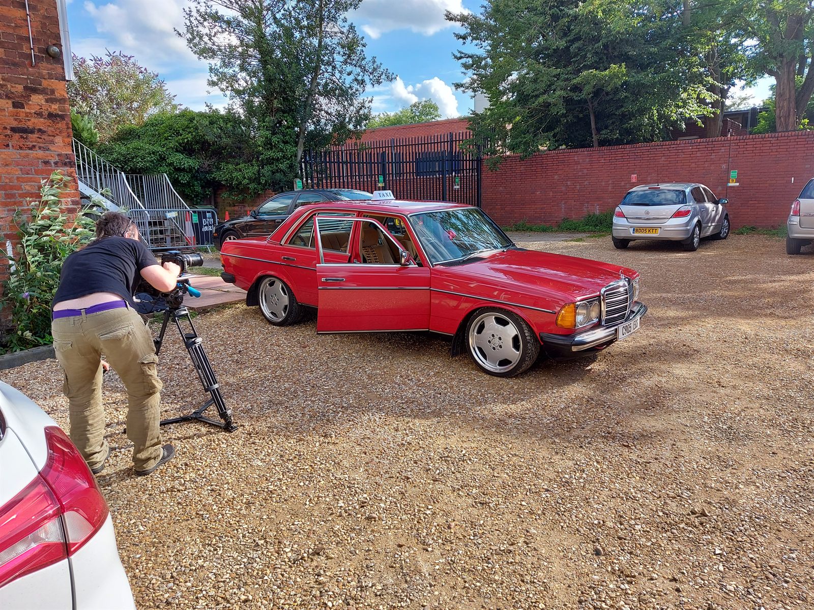 Camera operator filming the red Mercedes W123 with the door open during a shoot