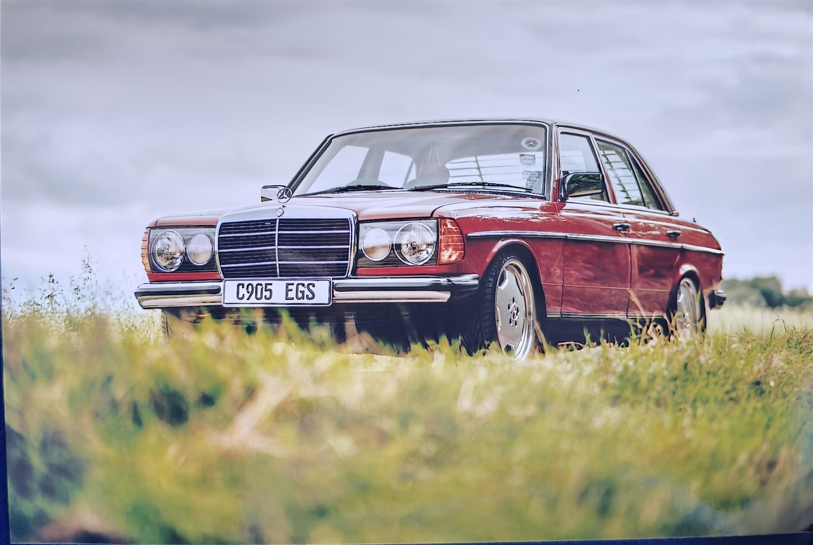 Red 1985 Mercedes-Benz W123, reg C905 EGS, parked in a summer field